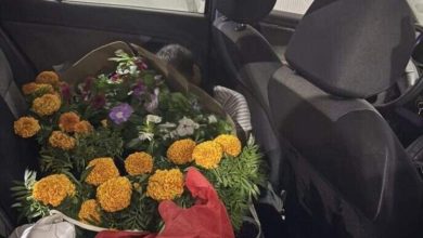 Bouquet of orange marigolds and other flowers wrapped in red paper on the back seat of a car.