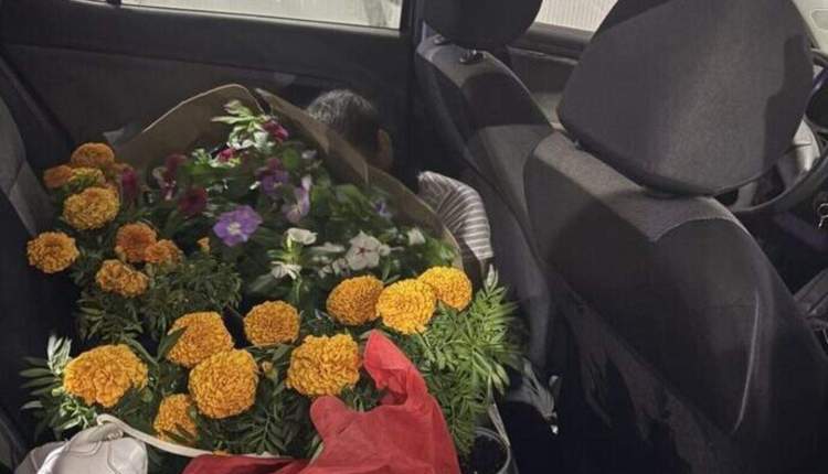 Bouquet of orange marigolds and other flowers wrapped in red paper on the back seat of a car.