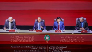 Four men in suits sit at a panel table on a stage, with a red backdrop and banners for the Moroccan Football Federation in Arabic and French behind them.