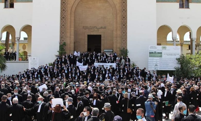 Large crowd of people, many in dark robes, gather on the steps of a grand arched entrance, holding protest banners during a demonstration at a historic building.