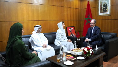 MAP6661 | MCG24 | موقع إلكتروني مغربي شامل متجدد على مدار الساعة Officials in traditional white robes and a woman in a light gray hijab sit on a leather sofa in a formal meeting room with a Moroccan flag nearby and a framed portrait on the wall.