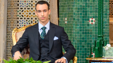 Moulay-El-Hassan1-1_jpg | MCG24 | موقع إلكتروني مغربي شامل متجدد على مدار الساعة Formal portrait of a man in a black suit and teal striped tie, seated on a gold chair beside a mosaic-tiled wall at an ornate setting.