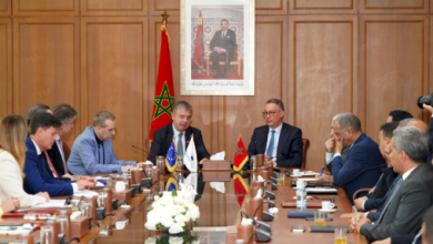 Formal diplomatic meeting with officials seated around a long wooden table; Moroccan and Turkish flags on the table and a portrait hanging on a paneled wall behind.
