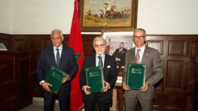 Nouveau-projet205 | MCG24 | موقع إلكتروني مغربي شامل متجدد على مدار الساعة Three men in suits stand side by side, each holding a green folder during an official ceremony, with a Moroccan flag behind them.