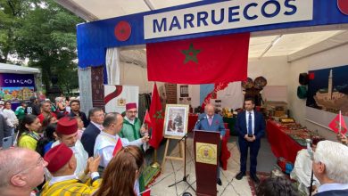 Nouveau-projet283 | MCG24 | موقع إلكتروني مغربي شامل متجدد على مدار الساعة Morocco booth at a cultural festival with a red Moroccan flag and a speaker at a podium addressing a crowd