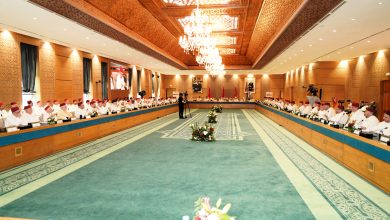 Nouveau-projet319 | MCG24 | موقع إلكتروني مغربي شامل متجدد على مدار الساعة Wide-angle view of a formal conference in a grand room, delegates in white attire and red caps seated around a long U-shaped table under a crystal chandelier.