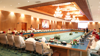 Formal meeting in a grand hall with delegates in white attire and red fez hats seated around a U-shaped table.