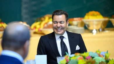 Prince-Moulay-Rachid | MCG24 | موقع إلكتروني مغربي شامل متجدد على مدار الساعة Smiling man in a black suit seated at a formal banquet table with colorful centerpieces in the foreground and fruit decor in the background.