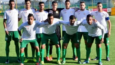 Rcaune_831510976 | MCG24 | موقع إلكتروني مغربي شامل متجدد على مدار الساعة Soccer team posing for a group photo on a grassy field, players in white jerseys and green shorts lined up in two rows before a match.