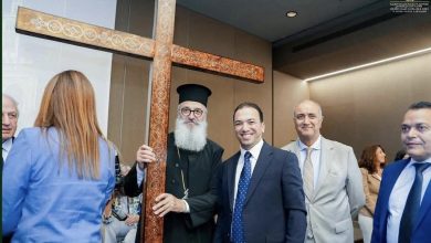 Group of formally dressed people posing indoors beside a large decorative wooden cross.