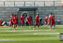 Snapshot | MCG24 | موقع إلكتروني مغربي شامل متجدد على مدار الساعة Soccer players in red uniforms running on a training field near a stone wall with a team logo backdrop.