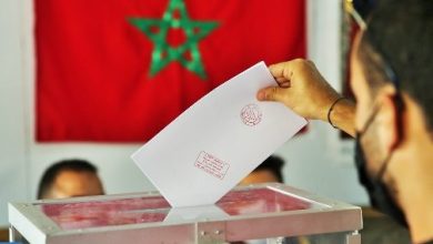 Vote-16-504x300-1 | MCG24 | موقع إلكتروني مغربي شامل متجدد على مدار الساعة Voter placing a ballot into a transparent ballot box at a polling station, with a red Moroccan flag in the background.