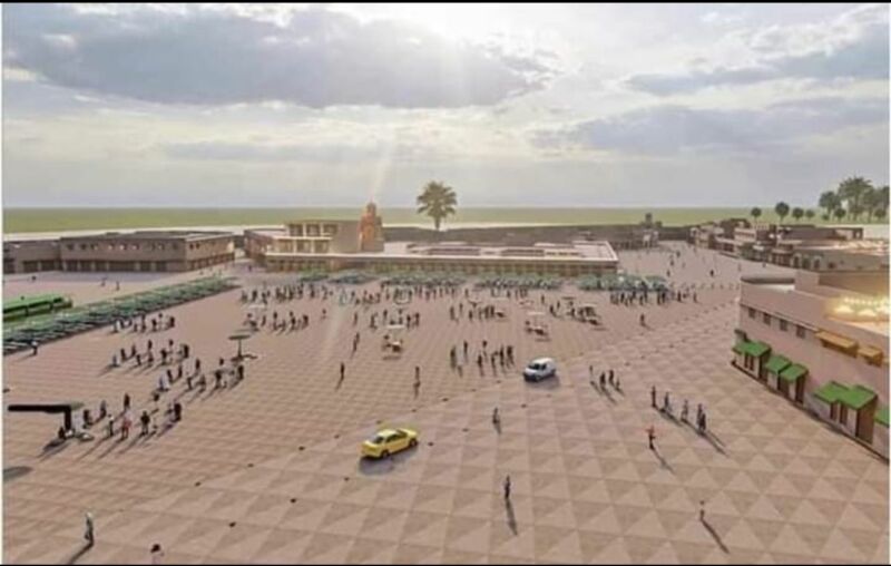 Wide view of a spacious coastal plaza with patterned tiles, people walking, a few cars, and low buildings along the edges.