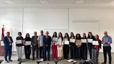 Group of people standing in a line, each holding certificates, posing for a photo in a bright room.