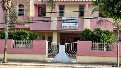 Front of a pink two-story building with a white gate and Arabic sign above the entrance