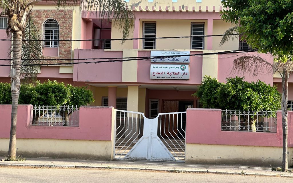 Front of a pink two-story building with a white gate and Arabic sign above the entrance