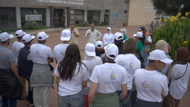 Group of people in white hats listening to two men speaking outside a police tourism office entrance.