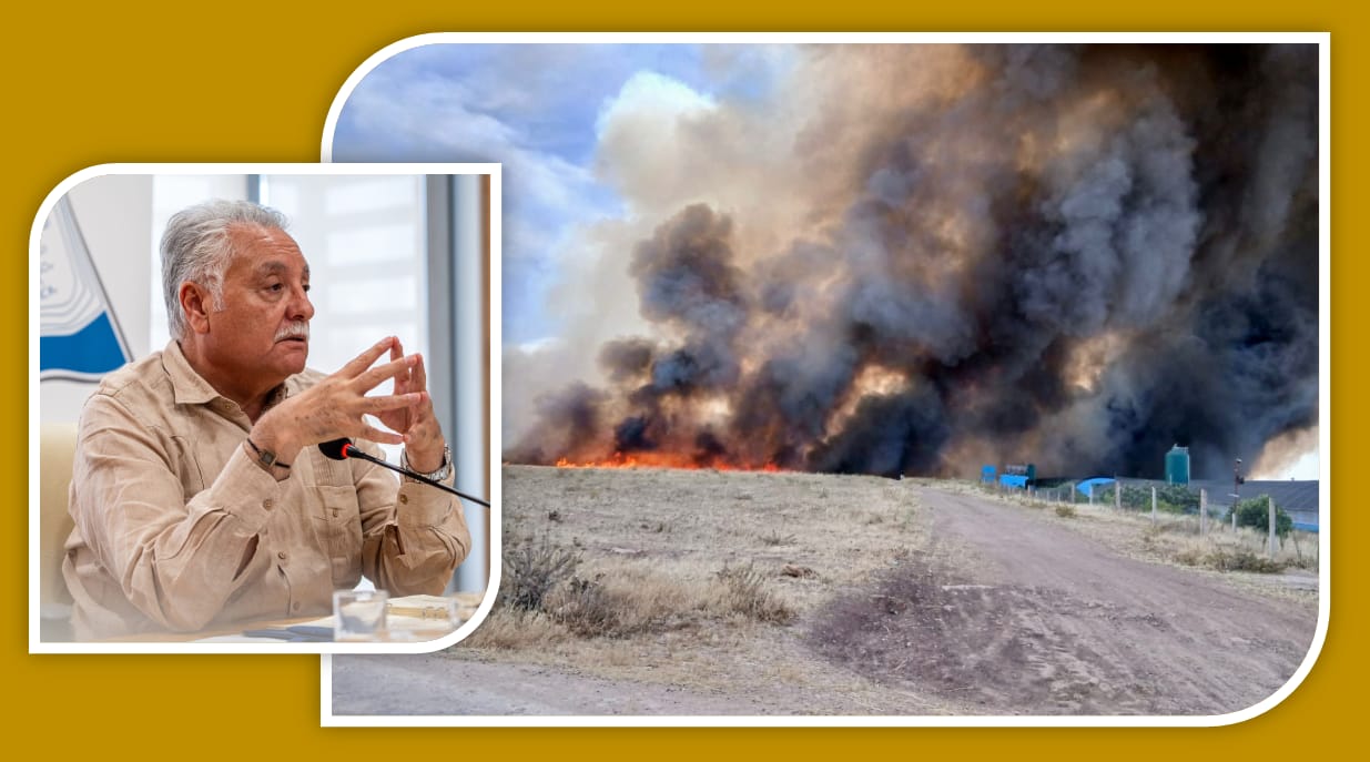 Man in a beige shirt speaking at a press conference; wildfire with smoke and flames on a rural dirt road behinds.