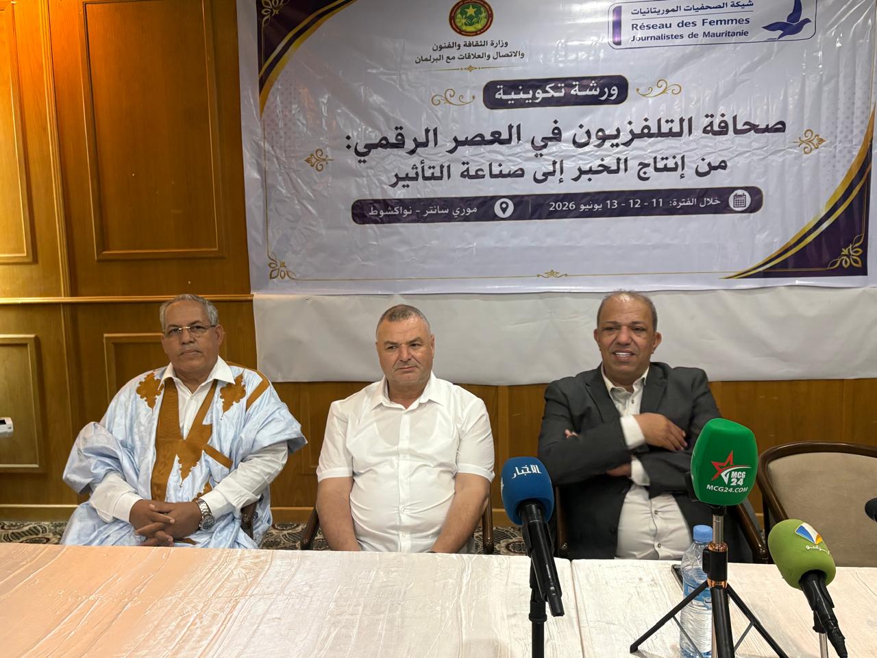 ثلاثة رجال يجلسون خلف طاولة في مؤتمر صحفي مع لافتة بالعربية عن ورشة تكوينية: صحافة التلفزيون في العصر الرقمي