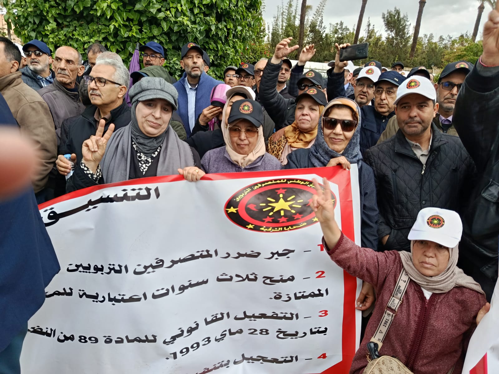 WhatsApp Image 2026-06-17 at 152451 1 | MCG24 | موقع إلكتروني مغربي شامل متجدد على مدار الساعة Crowd of protesters holding a banner with Arabic text and a circular emblem; several people raise their hands, some making peace signs.