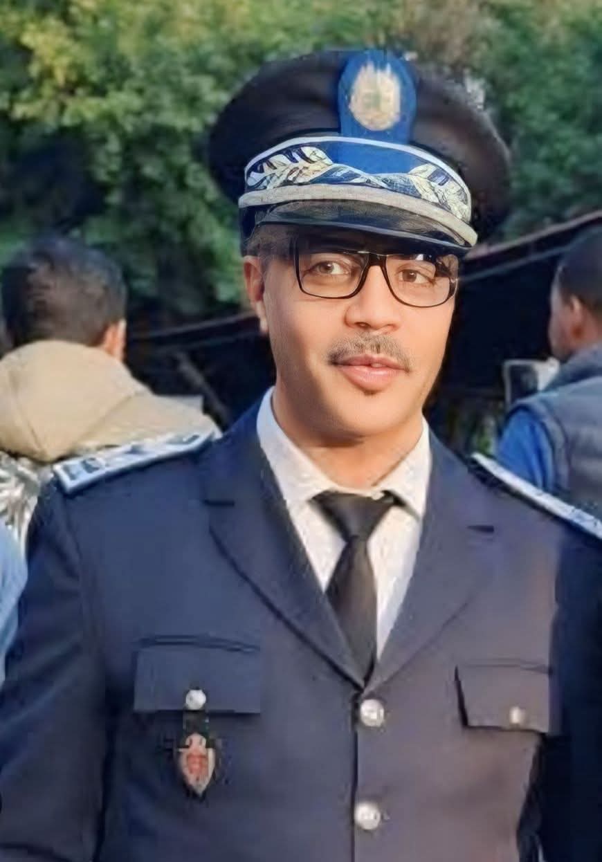 WhatsApp Image 2026-06-19 at 131917 | MCG24 | موقع إلكتروني مغربي شامل متجدد على مدار الساعة Young man in a formal police uniform with a blue cap, glasses, and tie, outdoors.