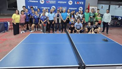 WhatsApp Image 2026-06-22 at 001436 | MCG24 | موقع إلكتروني مغربي شامل متجدد على مدار الساعة Group of young table tennis players and coaches posing for a photo behind a blue table tennis table inside a sports hall, with a branded backdrop featuring logos.