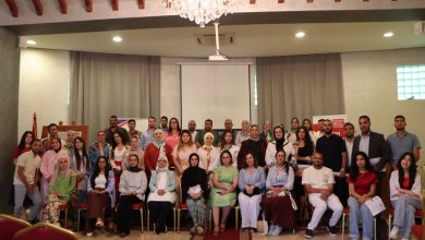 Large group of men and women posing for a group photo in a conference hall with a chandelier above.