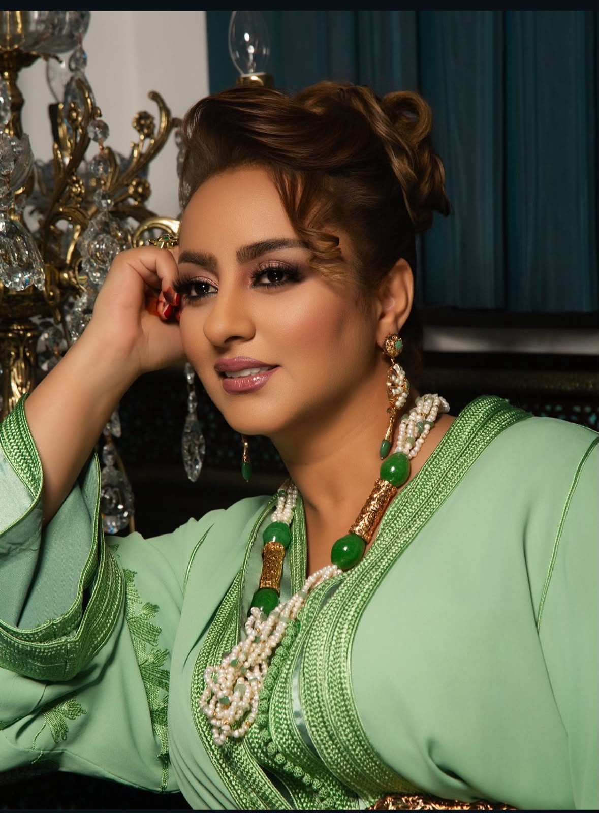 WhatsApp Image 2026-06-22 at 092648 | MCG24 | موقع إلكتروني مغربي شامل متجدد على مدار الساعة Portrait of a woman in a green traditional outfit, resting her head on her hand, wearing layered pearl and green bead jewelry.