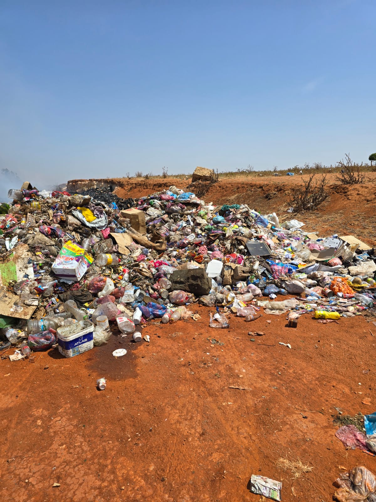 WhatsApp Image 2026-06-22 at 154548 | MCG24 | موقع إلكتروني مغربي شامل متجدد على مدار الساعة Pile of trash and litter on red dirt under a clear blue sky at a dumpsite.