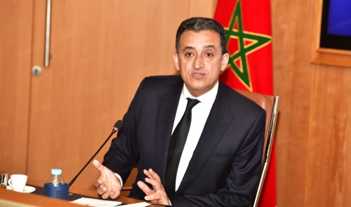Younes-Idrissi-Kaitouni-508x300-508x300-1 | MCG24 | موقع إلكتروني مغربي شامل متجدد على مدار الساعة Man in a dark suit speaks at a desk with a microphone, Moroccan flag visible in the background behind him.