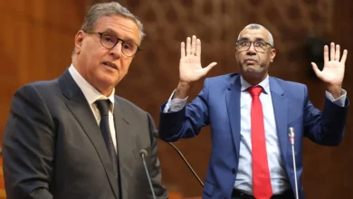 akh-et-bwanoujpg | MCG24 | موقع إلكتروني مغربي شامل متجدد على مدار الساعة Two men in suits at a podium; one speaks into a microphone while the other raises both hands in a gesture.