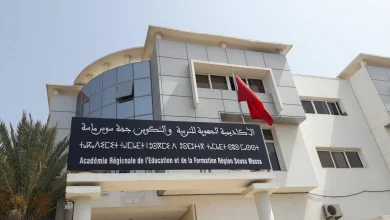 arefs-001-optimisee | MCG24 | موقع إلكتروني مغربي شامل متجدد على مدار الساعة Modern white education building with a large black sign in Arabic and French, a red flag, and palm trees on the left.