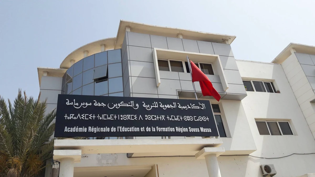 arefs-001-optimisee | MCG24 | موقع إلكتروني مغربي شامل متجدد على مدار الساعة Modern white education building with a large black sign in Arabic and French, a red flag, and palm trees on the left.