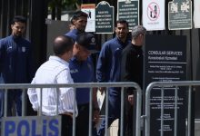 Police officers in blue uniforms behind metal barricades outside a consular services sign area, Turkish 'POLIS' lettering visible in foreground.