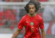 bouaadi-2 1 | MCG24 | موقع إلكتروني مغربي شامل متجدد على مدار الساعة Footballer in a red Morocco jersey with number 6, focused on the game with long curly hair and a white headband on the field.