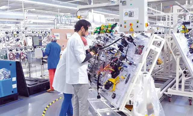 cablagejpg | MCG24 | موقع إلكتروني مغربي شامل متجدد على مدار الساعة Technician in a white coat and mask repairing a complex electrical control panel on an assembly line in a bright factory.
