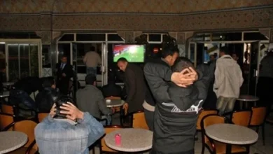 cafemaroc_129458349 | MCG24 | موقع إلكتروني مغربي شامل متجدد على مدار الساعة Group of men in a casual lounge watching a football match on a TV; some lean back with hands on their heads in frustration while seated at small tables.