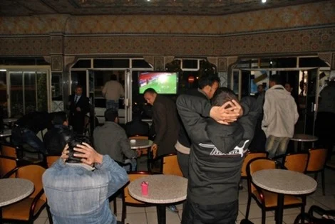 cafemaroc_129458349 | MCG24 | موقع إلكتروني مغربي شامل متجدد على مدار الساعة Group of men in a casual lounge watching a football match on a TV; some lean back with hands on their heads in frustration while seated at small tables.