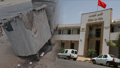 cdccddc | MCG24 | موقع إلكتروني مغربي شامل متجدد على مدار الساعة Collapsed concrete structure leaning into the street beside a hotel building with a red flag overhead, showing damage and debris on the road.