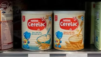 Two cans of Nestlé Cerelac infant cereal on a store shelf: Rice with Milk and Wheat with Milk side by side.