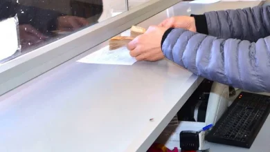 change-argent | MCG24 | موقع إلكتروني مغربي شامل متجدد على مدار الساعة Person in a blue jacket wipes or brushes a document on a service counter beneath a glass divider at a reception or teller desk.