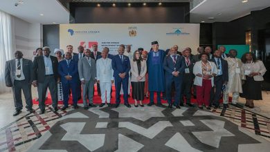 fettah-banque-shelter768vd | MCG24 | موقع إلكتروني مغربي شامل متجدد على مدار الساعة Group of professionals in formal attire posing for a group photo at a conference, with a banner featuring Shelter Afrique logos behind them.