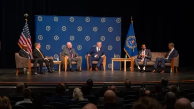 fifa-FBI | MCG24 | موقع إلكتروني مغربي شامل متجدد على مدار الساعة Six men in suits sit on stage in a panel discussion, with U.S. flag and blue emblem backdrop behind them; audience in foreground.