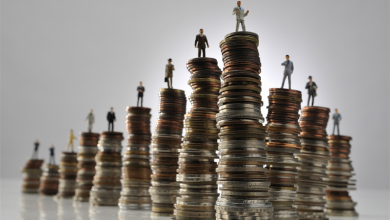 fortune-plus-riches | MCG24 | موقع إلكتروني مغربي شامل متجدد على مدار الساعة Miniature businesspeople stand on stacked coins of varying heights, illustrating the financial ladder and progression.