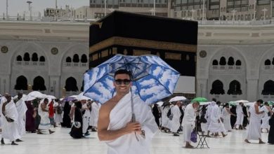 hamdallah | MCG24 | موقع إلكتروني مغربي شامل متجدد على مدار الساعة Smiling man in white ihram holding a blue sky umbrella in the courtyard of the Kaaba, with pilgrims around.