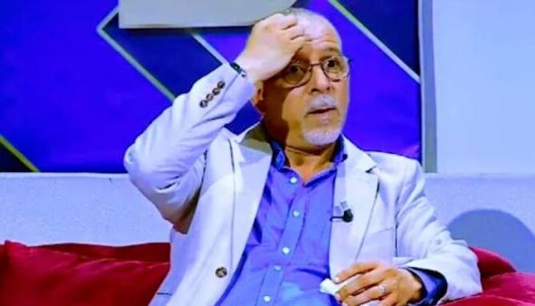 images | MCG24 | موقع إلكتروني مغربي شامل متجدد على مدار الساعة Man on a TV talk show sits on a red couch, hand on forehead, wearing a light blazer and glasses.
