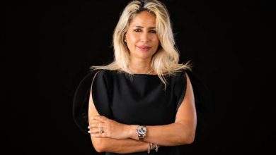images | MCG24 | موقع إلكتروني مغربي شامل متجدد على مدار الساعة Professional woman with blonde hair in a black dress, arms crossed, against a dark background.