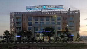 2154545 | MCG24 | موقع إلكتروني مغربي شامل متجدد على مدار الساعة Modern hotel building with brick façade, glass windows, and a blue-lit entrance at dusk, with trees lining the front.