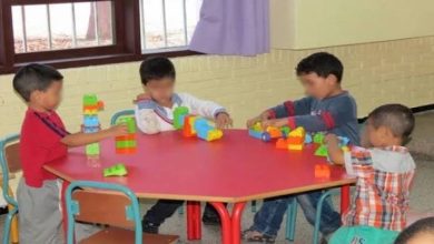 images 44 | MCG24 | موقع إلكتروني مغربي شامل متجدد على مدار الساعة Four young children sit around a pink round table, stacking colorful plastic blocks in a classroom setting.