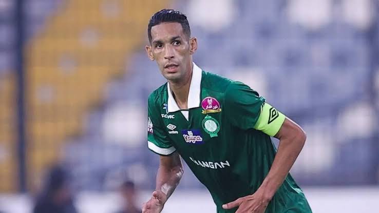 images | MCG24 | موقع إلكتروني مغربي شامل متجدد على مدار الساعة Soccer player in a green jersey with a yellow captain's armband, mid-match on the pitch.
